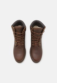 Botas de tobillo de cuero marrón con un acabado suave, puntera redonda, cordones color tostado y un cuello acolchado negro. Presenta el logo en la lengüeta y en el lateral.