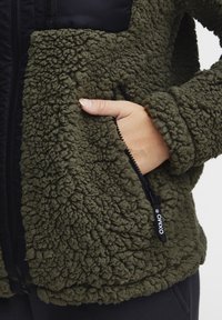 Groene synthetische fleecedubbel jacket met een getextureerde, pluizige buitenkant en een ritszak met zwarte hardwareaccenten.