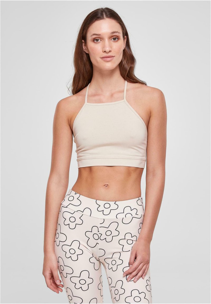Halyu beige vaatepaita, joka on valmistettu pehmeästä materiaalista, yhdistettynä tiukkoihin leggingseihin, joissa on musta kukkakuosi vaalean kermanvärisellä taustalla.