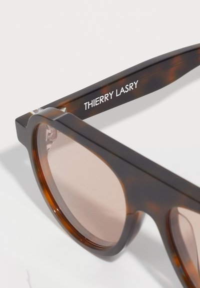 Occhiali da sole tartarugati marroni con lenti rettangolari e montatura spessa e lucida. Il braccio presenta il testo "THIERRY LASRY" in bianco.