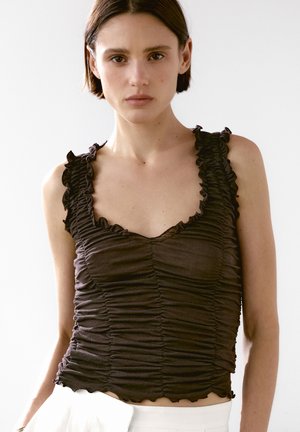 Brown ruched tank top with scalloped edges and ruffled straps, featuring a fitted design and soft texture, worn over white bottoms.