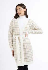 Strickjacke in Creme und Beige mit einem strukturierten Muster, V-Ausschnitt, langen Ärmeln und einem Bindedetail. Mit zwei frontalen Taschen.