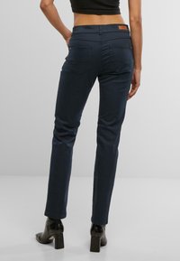 Jeans ajustados de color azul oscuro, confeccionados en denim, con una cintura de altura media, bolsillos traseros y una etiqueta de marca de cuero marrón en la cintura.