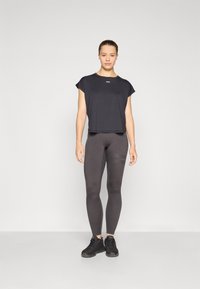 Black cropped t-shirt with short sleeves, paired with dark gray leggings featuring striped accents. Worn with black athletic shoes.