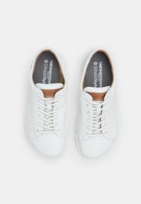White leather sneakers with a smooth texture, brown leather accents near the laces, and beige laces. Gray insoles feature logo text.
