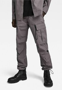Šedé cargo kalhoty s několika kapsami, detailem na šňůrku a zúženým střihem, spárované s černými šněrovacími botami pro zvýraznění kontrastu.