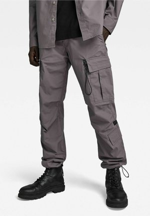 Grijze cargo pants met meerdere zakken, een trekkoorddetail en een taps toelopende pasvorm, gecombineerd met zwarte veterschoenen voor extra contrast.