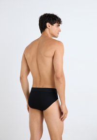Čierne slipy strihu briefs s jednofarebným, bezšvovým dizajnom a mäkkým elastickým pásom, zobrazené na modeli zozadu.