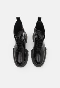 Zwarte glanzende enkellaarzen met een gestructureerde rubberen zool, voorzien van een vetersluiting aan de voorkant en een ritssluiting aan de zijkant.