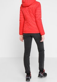 Červená prošívaná bunda s kapucí, s diagonálními švy. V kombinaci s černými slim-fit džíny a černými botami s červenými akcenty.