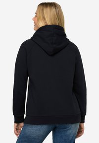 Sudadera con capucha azul marino de acabado texturizado, con mangas raglán y un bolsillo tipo canguro, combinada con jeans rayados azul claro.