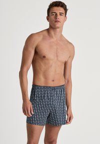 Herenboxers in donkerblauw met een herhalend wit patroon van abstracte vormen. De stof lijkt lichtgewicht en heeft een elastische tailleband.