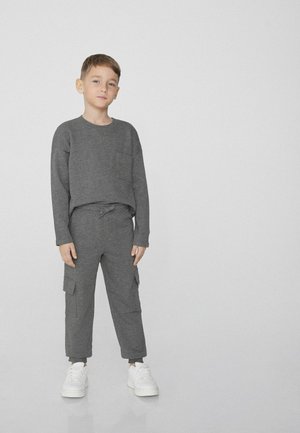 Graues Langarmshirt mit Tasche, kombiniert mit passenden Cargo-Hosen mit Seitentaschen und einem Kordelzugbund, ergänzt durch weiße Sneakers.