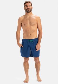 Modre kopalne hlače z zelenim vrvico za zavezovanje, stranskimi žepi in majhno logotipno značko. Mehka tkanina, dolžina do sredine stegen in klasičen kroj.