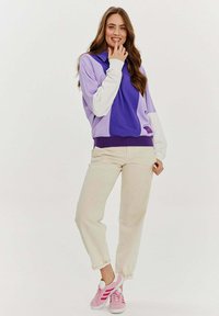 Fioletowo-biała bluza w kolorze bloków o luźnym kroju, zestawiona z beżowymi spodniami taper oraz różowymi sneakerami z białymi akcentami.