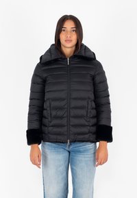 Giubbotto piumino nero con zip frontale, texture a coste, ampio colletto e polsini in pelliccia sintetica nera. Presenta dettagli cuciti e una forma leggermente aderente.