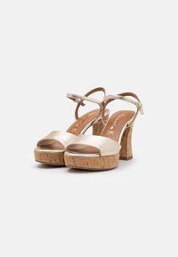 Metallic gold platform sandals with a cork heel, open toe design, and adjustable ankle strap. Smooth upper with a textured cork base.