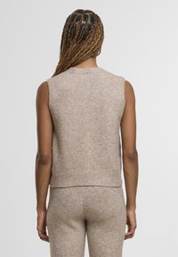 Béžový svetr bez rukávů s kulatým výstřihem, měkkou texturou a žebrovaným lemem. Má přiléhavý střih a minimalistický design.