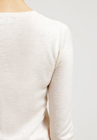 Pull en maille beige clair avec une texture douce, un col rond et des manches longues. Vue de dos, révélant un design simple et sans coutures.