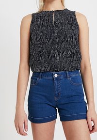 Marinblus utan ärmar med vitt prickigt mönster och nyckelhålsdetalj, tillsammans med hög midja denimshorts i mörkblått med uppvikta fållar.