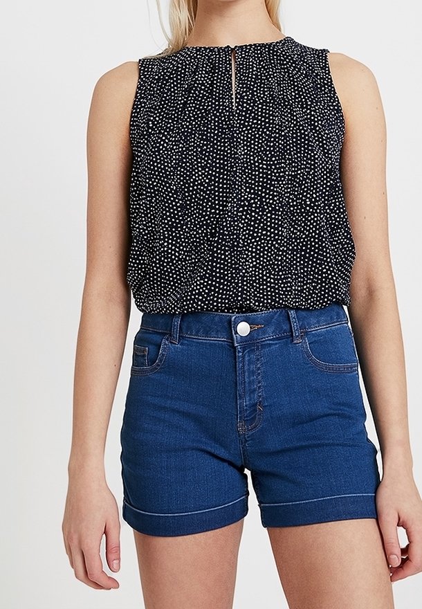 Marinblus utan ärmar med vitt prickigt mönster och nyckelhålsdetalj, tillsammans med hög midja denimshorts i mörkblått med uppvikta fållar.