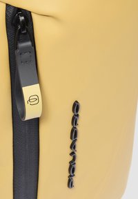 Borsa impermeabile gialla con cerniera nera e linguetta, caratterizzata da logo in rilievo lungo il lato e superficie liscia e testurizzata.