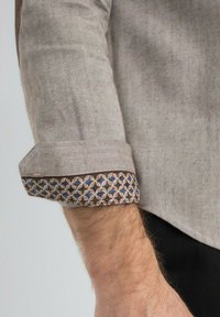 Chemise beige à motif en chevrons avec un poignet arborant un design géométrique bleu, marron et crème. Tissu en coton avec une texture lisse.