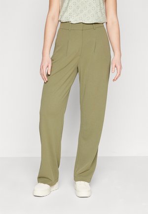 Green, wide-leg trousers made from a smooth fabric with pleated front design. Fitted at the waist, paired with white sneakers.