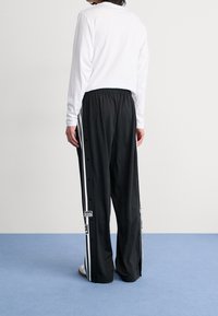 Svarta träningsbyxor med vita sidosträck och tryckknappdetaljer, i kombination med en långärmad vit skjorta. Slät textur, avslappnad passform.