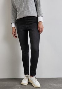 Grå tröja med uppvikt ärm, svarta slim-fit jeans och vita sneakers. Släta texturer, avslappnad design och rena linjer.