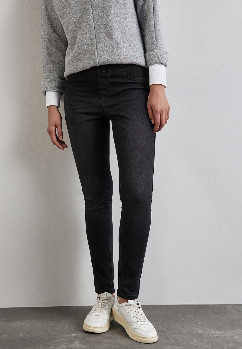 Grå tröja med uppvikt ärm, svarta slim-fit jeans och vita sneakers. Släta texturer, avslappnad design och rena linjer.