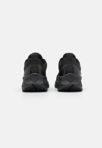 Zapatillas deportivas negras con parte superior de malla, suela de goma y tiradores en la parte trasera, con un diseño aerodinámico y curvado.