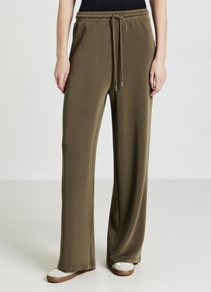 Pantaloni a gamba larga verde oliva in un tessuto liscio, caratterizzati da una vita elastica con cordoncino e una leggera lucentezza, abbinati a scarpe di colore chiaro.