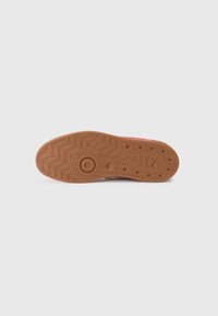 Gummisål til sneakers med et tekstureret bølgemønster i tan. Har cirkulære indrykninger og et trykt logo nær hælen.