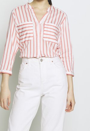 Camicetta a righe rosa e bianche con colletto, due tasche sul petto e maniche lunghe, abbinata a jeans bianchi a vita alta.