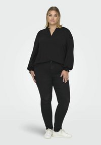 Černá blůza s dlouhým rukávem, výstřihem do V a nařasenými manžetami, kombinovaná s černými skinny džíny a bílými teniskami. Hladký materiál, volný střih.