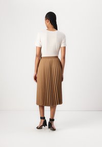 Beige pleated skirt in lightweight fabric, with a fitted waistband, paired with a plain short-sleeve top and black strapped heels.