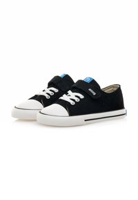Zapatillas de lona negras con una suela de goma blanca, que presentan cierre de cordones y con velcro, una etiqueta azul en la lengüeta y acentos a rayas en blanco y negro.