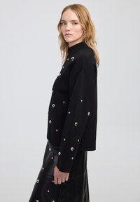 Maglione nero con collo alto, decorato con borchie argentate, dotato di maniche lunghe e una vestibilità comoda. Tessuto a maglia testurizzato.