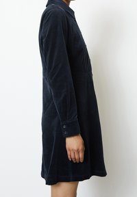 Abito camicia in corduroy blu navy con colletto, apertura con bottoni, maniche lunghe e una silhouette svasata che arriva sopra il ginocchio.