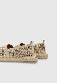 Zapatos tipo espadrille beige sin cordones con parte superior de ante perforado, suela envuelta en yute y lengüetas en el talón sobre un fondo claro.