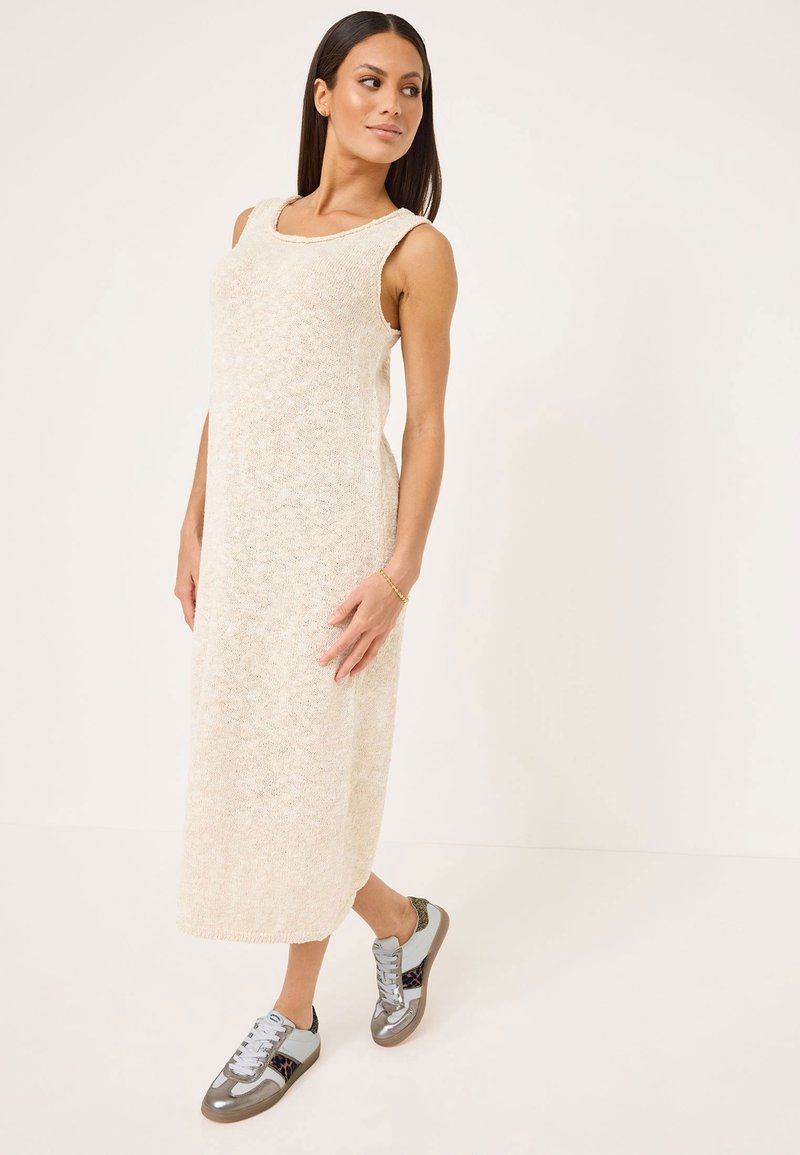 Abito lungo senza maniche beige in maglia con scollo tondo; indossato con sneakers grigie e blu con accenti metallici e dettagli texturizzati.
