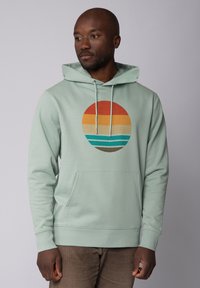Mintgroene hoodie met een centrale graphic van een zonsondergang in oranje en blauwe tinten, met een voorzak en verstelbare trekkoorden.