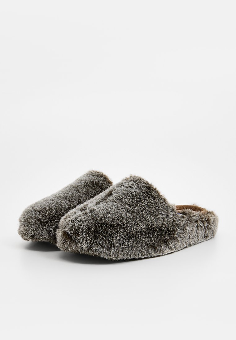 Chaussons en fausse fourrure avec un extérieur doux et gris, un design à bout arrondi, et sans fermeture visible. L'intérieur semble rembourré pour plus de confort.