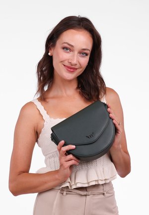 Grüne Kunstleder-Crossbody-Tasche mit einer gewölbten Klappe, ausgestattet mit einem metallischen Logoakzent und einem Reißverschluss, in den Händen vor einem hellen Hintergrund gehalten.
