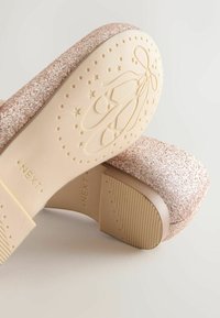 Mirdzoša rozā augstpapēžu kurpe ar masīvu formu. Ievērojama ar gludu gaismas pamatu un reljefu baleta kurpju dizainu uz zoles.