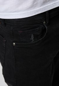 Jeans negri din denim, cu un design standard cu cinci buzunare, cusături roșii subtile și un mic logo brodat pe buzunarul din spate.