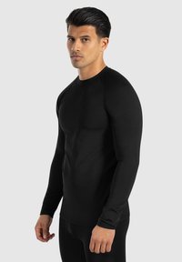 Schwarzes Langarmshirt in taillierter Passform, mit Rundhalsausschnitt und glatter Textur, getragen von einem männlichen Model vor neutralem Hintergrund.