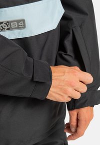 Czarna kurtka z jasnoniebieską wstawką, naszywką z logo i kieszenią na zamek, o gładkiej teksturze i dopasowanych mankietach.