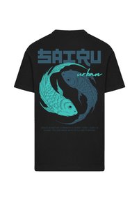 Black t-shirt featuring turquoise koi fish graphic, text "Saitru" above, and slogan below. Design includes flowing lines and detailed scales.